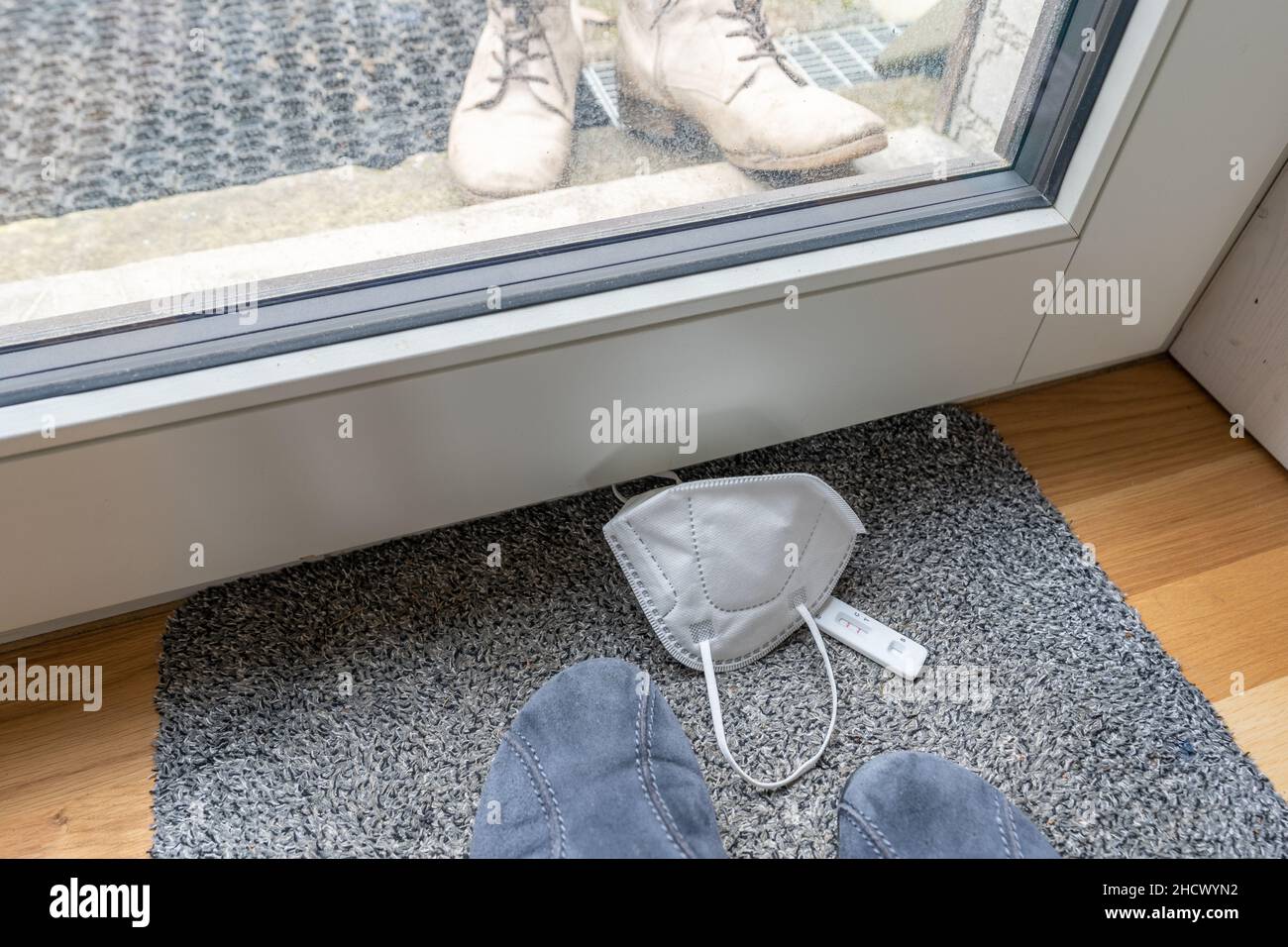 High-Angle-Ansicht von Haus Hausschuhe und Stiefel im Freien mit positiven Selbsttest und Schutzmaske auf dem Boden. Stockfoto