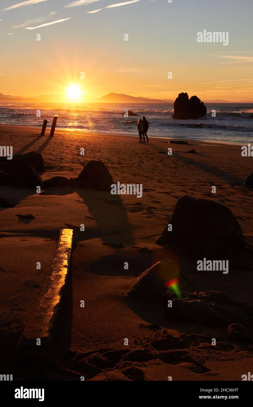 Landschaft eines Sonnenuntergangs, die Sonne versteckt sich im Hintergrund über dem Meer und hinterlässt warme Orange-Töne auf dem Sand des Strandes, mehrere Felsen schaffen eine Idylle Stockfoto