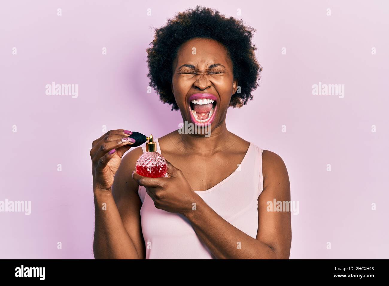Junge afroamerikanische Frau, die Parfüm zornig und wütend hält, schreit frustriert und wütend, schreit mit Wut, die aufschaut. Stockfoto