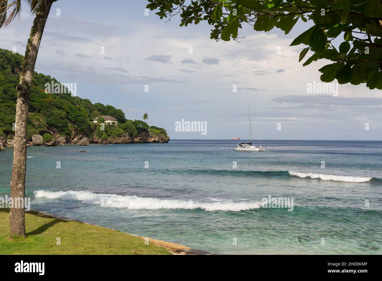 Kleine Wellen brechen in die Flying Fish Cove ein, während eine Yacht dahinter auf Christmas Island festgemacht wird. Stockfoto