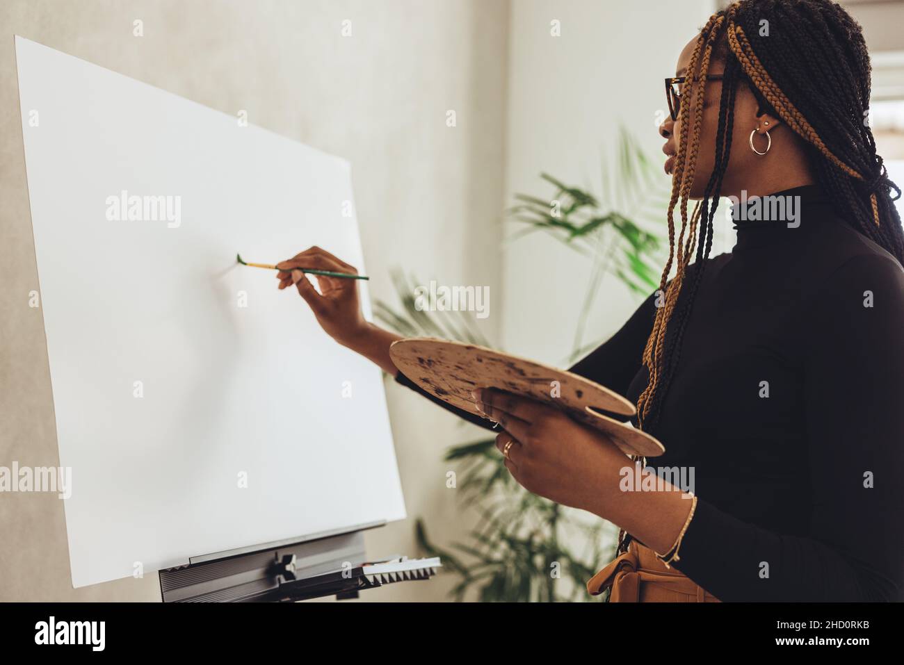 Junge Malerin zeichnet in ihrem Atelier. Kreative Malerin, die eine Palette hält, während sie vor einer Leinwand steht. Freischaffender Künstler Stockfoto