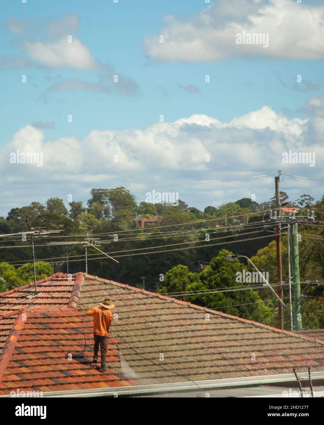 Mann, der im Surburban Sydney mit einem Hochdruckreiniger Flechten und Moos vom Terrakotta-Ziegeldach reinigte Stockfoto