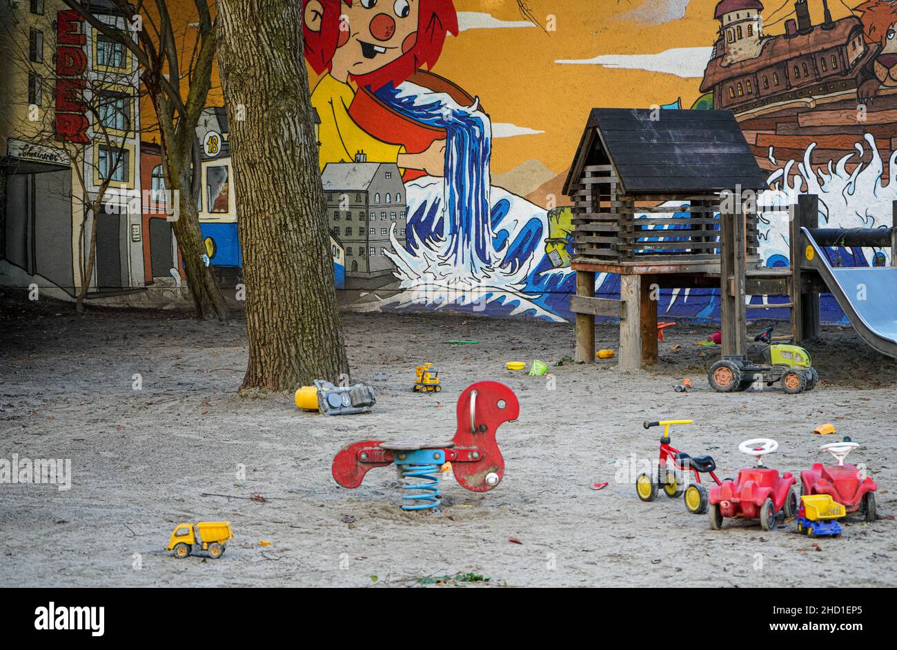 Kinderspielplatz in einer Stadt, mit zahlreichen Spielsachen, Sandkasten und Rutsche vor einer Wand mit bunten Straßenkunst Stockfoto