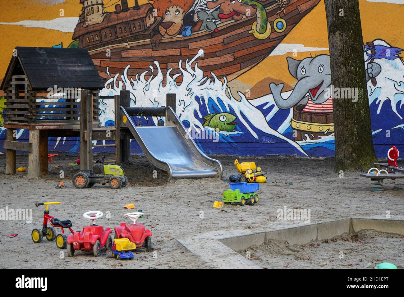 Kinderspielplatz in einer Stadt, mit zahlreichen Spielsachen, Sandkasten und Rutsche vor einer Wand mit bunten Straßenkunst Stockfoto