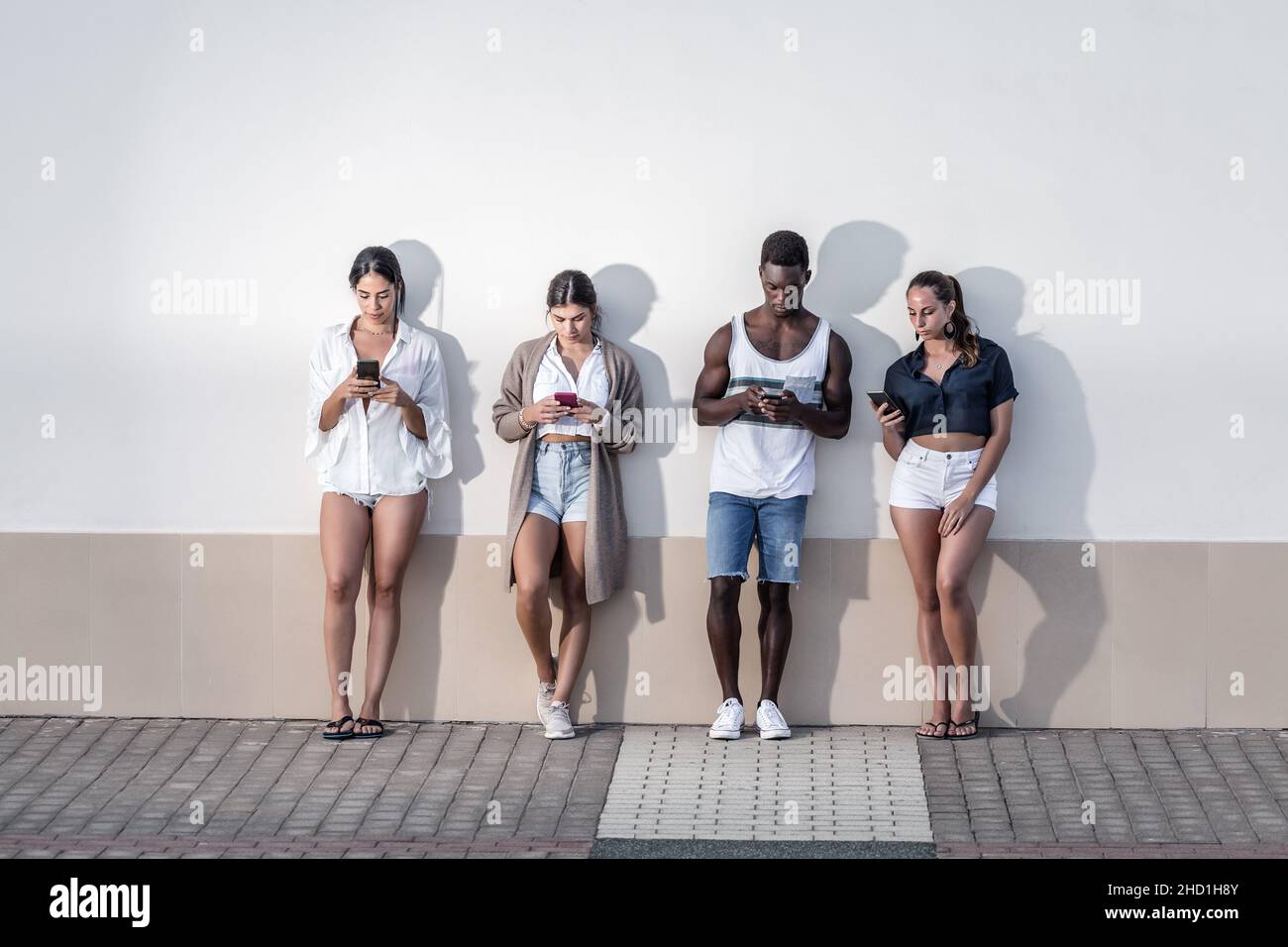 Unternehmen von multiethnischen Freunden, die in der Nähe von Gebäuden in der Stadt stehen und Mobiltelefone surfen, während sie ein Wochenende auf Lanzarote verbringen Stockfoto