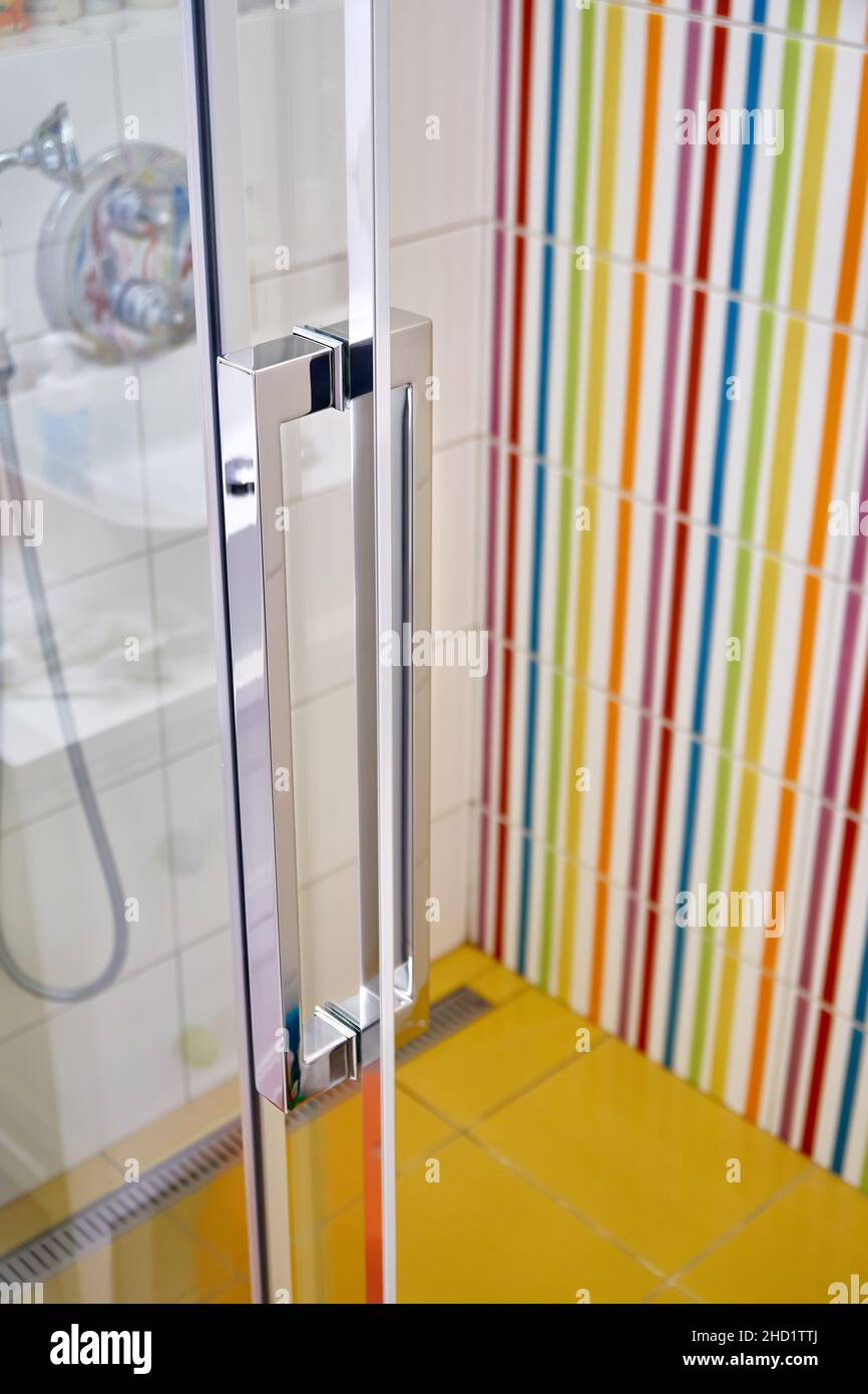 Geschlossene Glastür mit stilvollem Metallgriff der modernen Duschkabine im Badezimmer mit bunten Fliesen an der Wand aus der Nähe Stockfoto