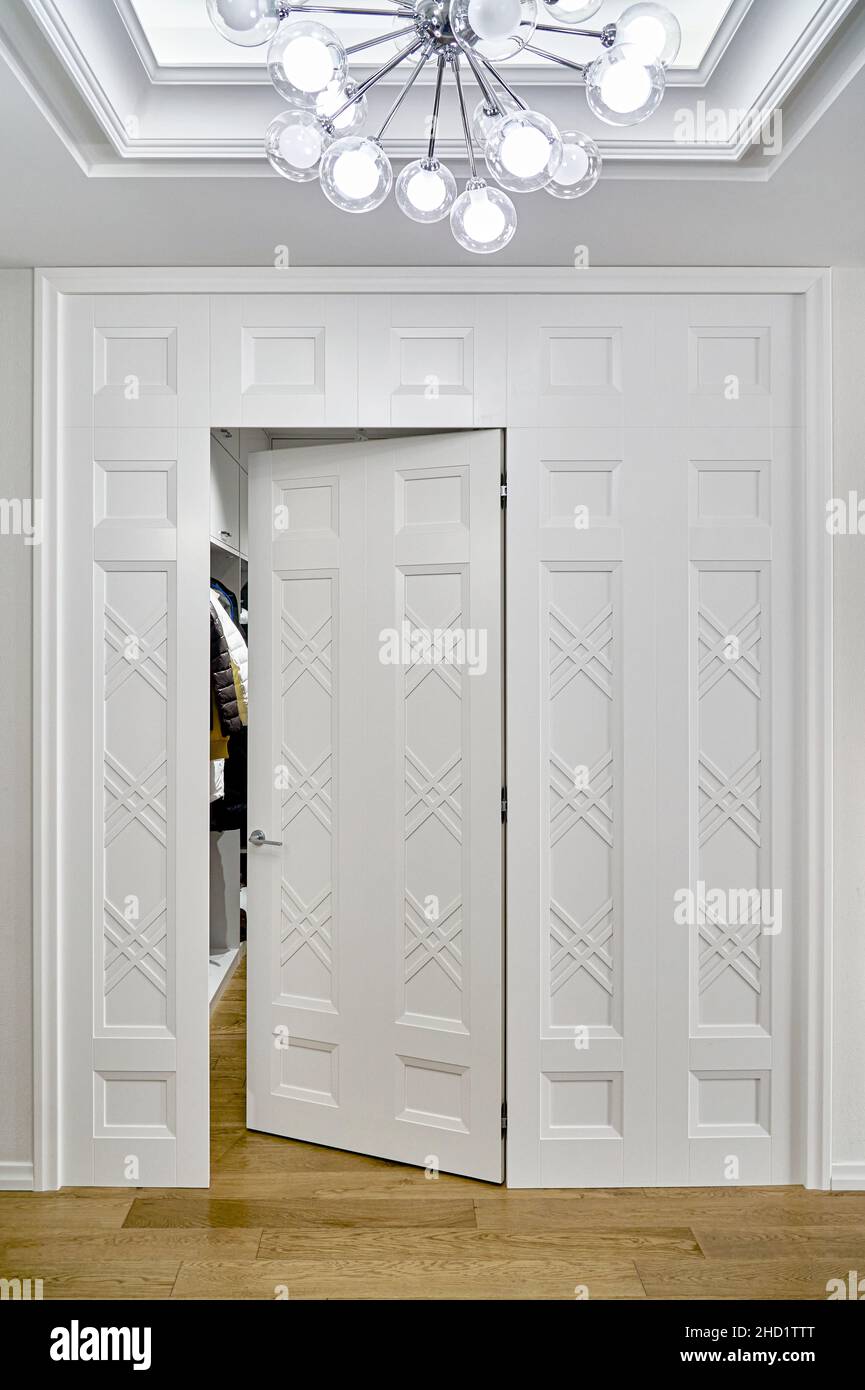 Stilvoller begehbarer Schrank, der durch eine elegante Wandverkleidung mit offener Tür vom hellen Eingangsbereich getrennt ist, in einem stilvoll renovierten Apartment Stockfoto