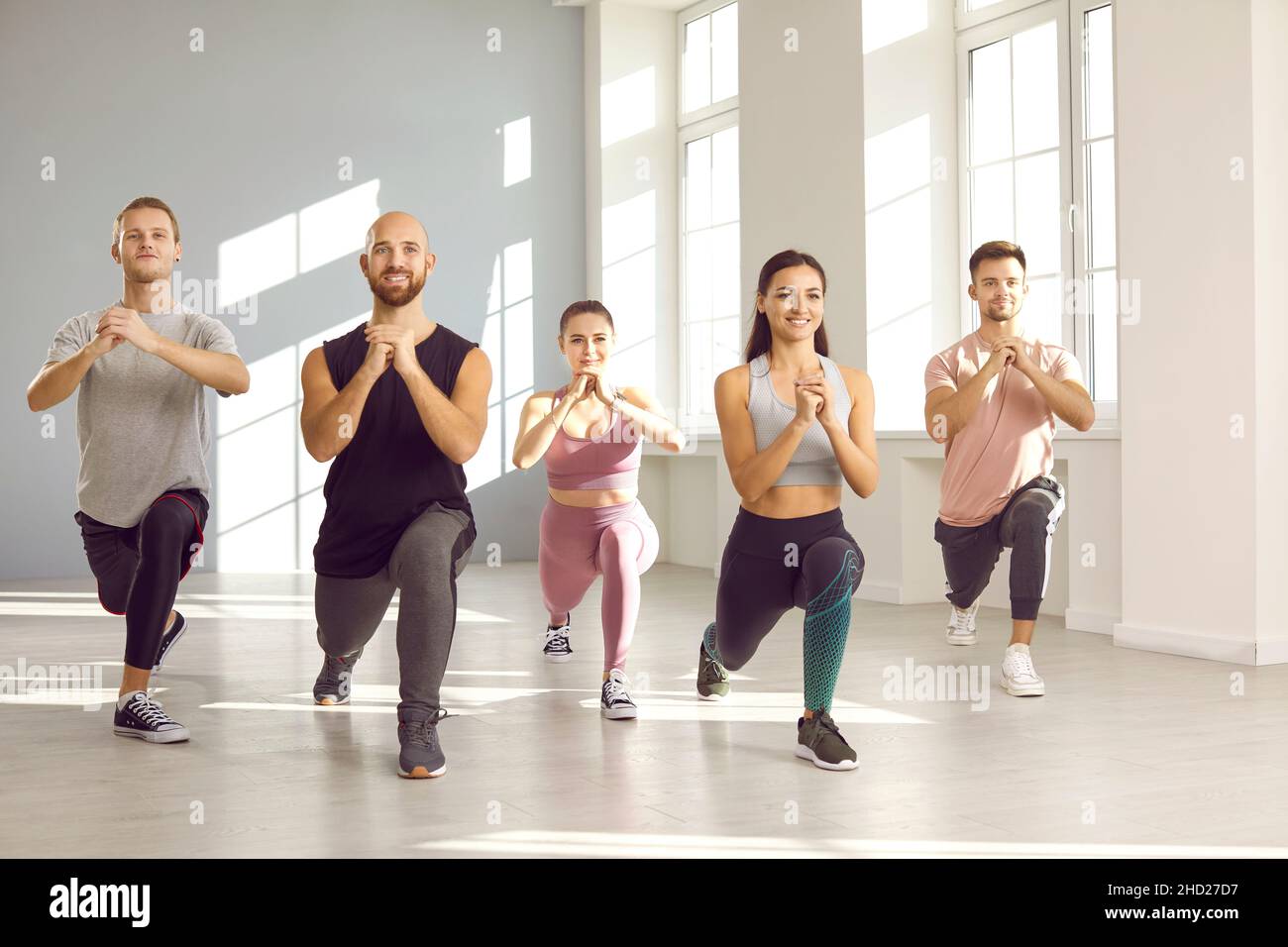 Junge aktive Menschen im Gruppentraining führen gemeinsam Beinübungen im hellen Fitnessstudio durch. Stockfoto