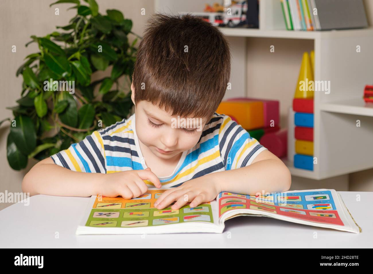 Ein 4-jähriges Kind sitzt an einem Tisch und liest ein Buch, schaut sich Bilder an, lernt lesen. Stockfoto