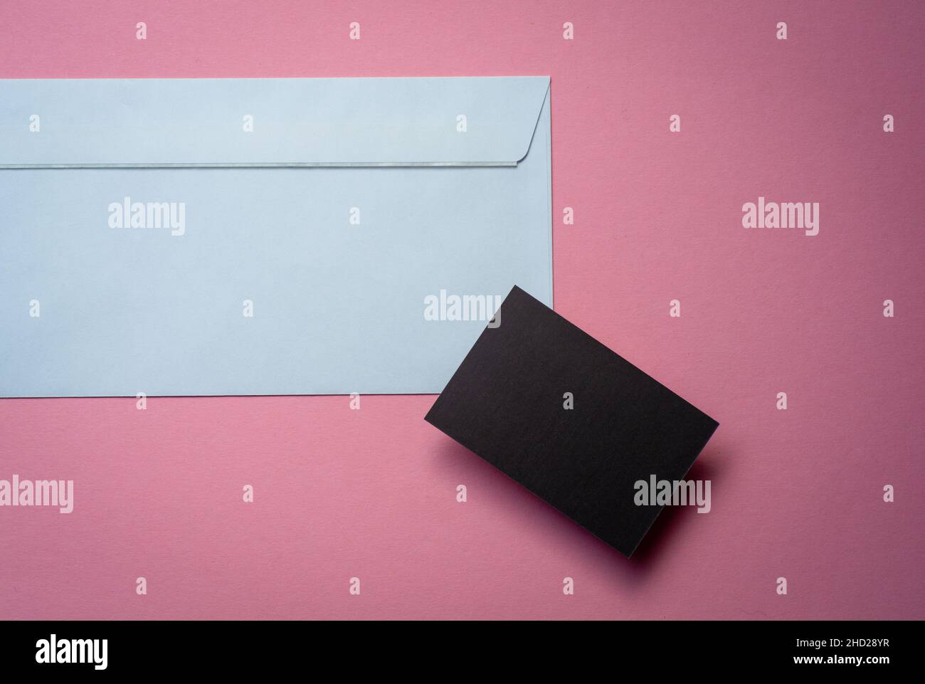 Schwarze imitierte Visitenkarte mit weißem Umschlag auf pinkem Hintergrund. Platz zum Kopieren für Ihr Design. Stockfoto