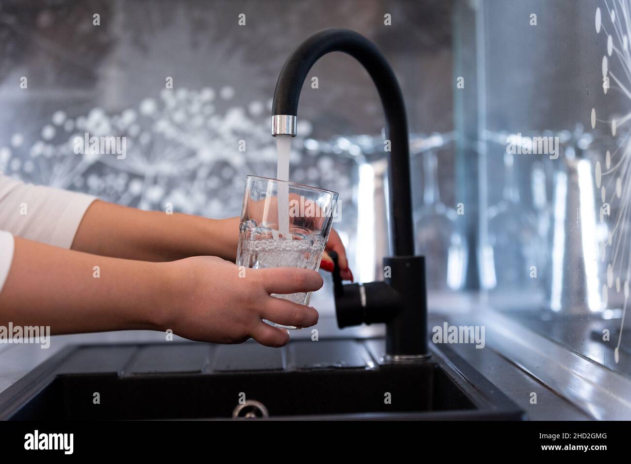 Hände einer jungen Frau, die ein Glas Wasser in eine moderne Küche gießt Stockfoto
