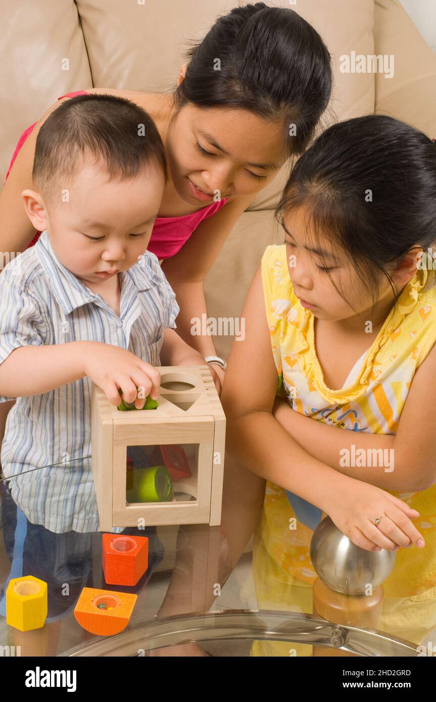 Vietnamesisch-amerikanische Familie zu Hause Kleinkind Junge spielt mit Form Sortierer, mit jungen Tante und 8-jährige Tante zu suchen Stockfoto