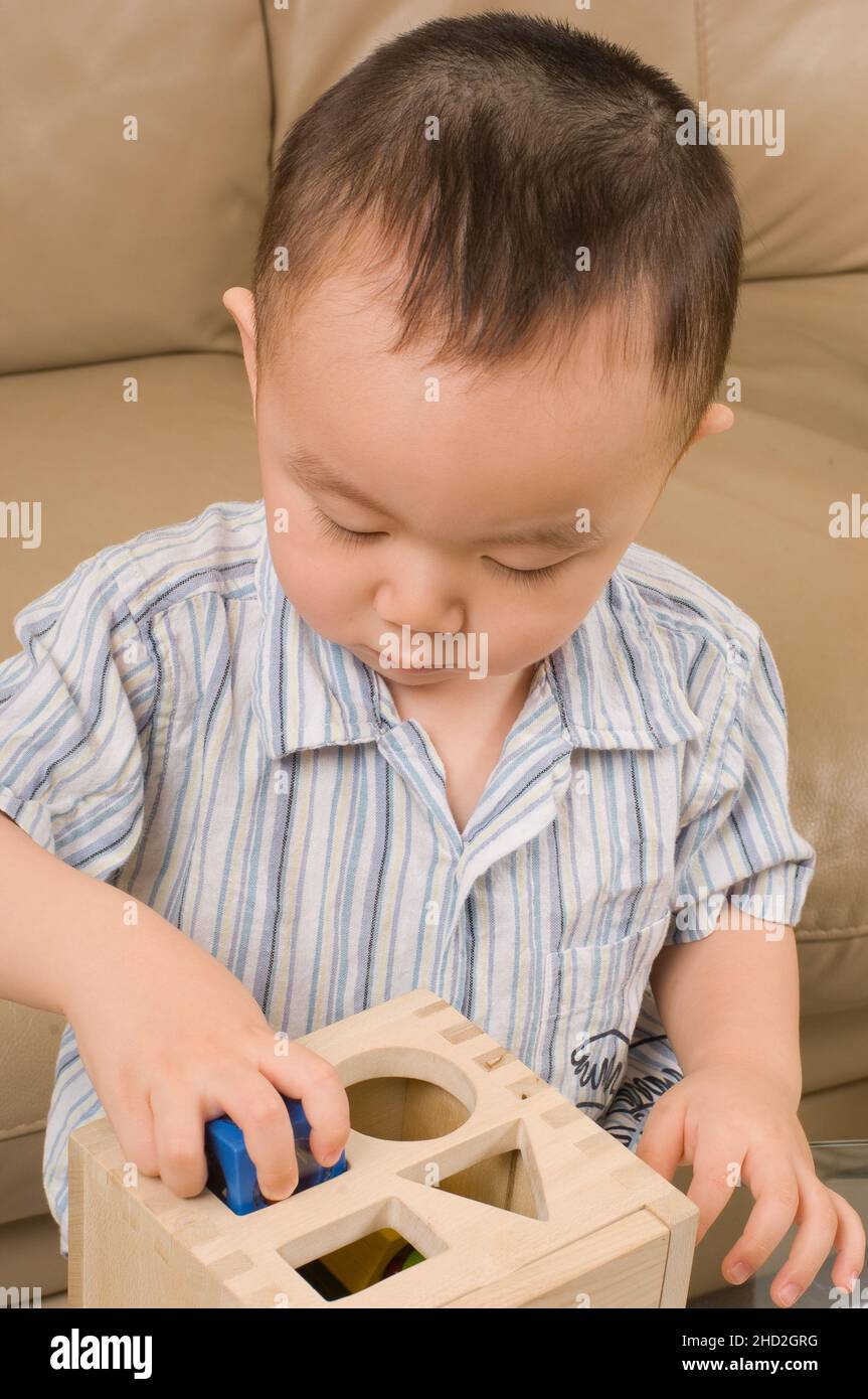 Vietnamesische amerikanische Familie zu Hause Kleinkind Junge spielt mit geometrischen Form Sortierer, passende Form in Loch Stockfoto