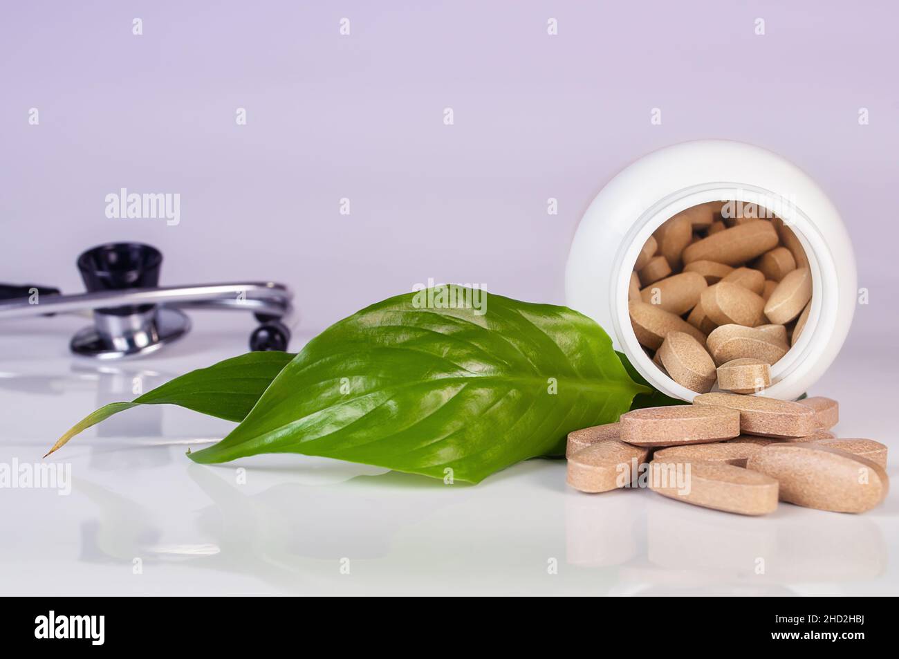 Weiße Botle mit Kräutertabletten, Stethoskop und grünen Blättern auf hellblauem Hintergrund aus nächster Nähe. Konzept der Kräutermedizin Stockfoto