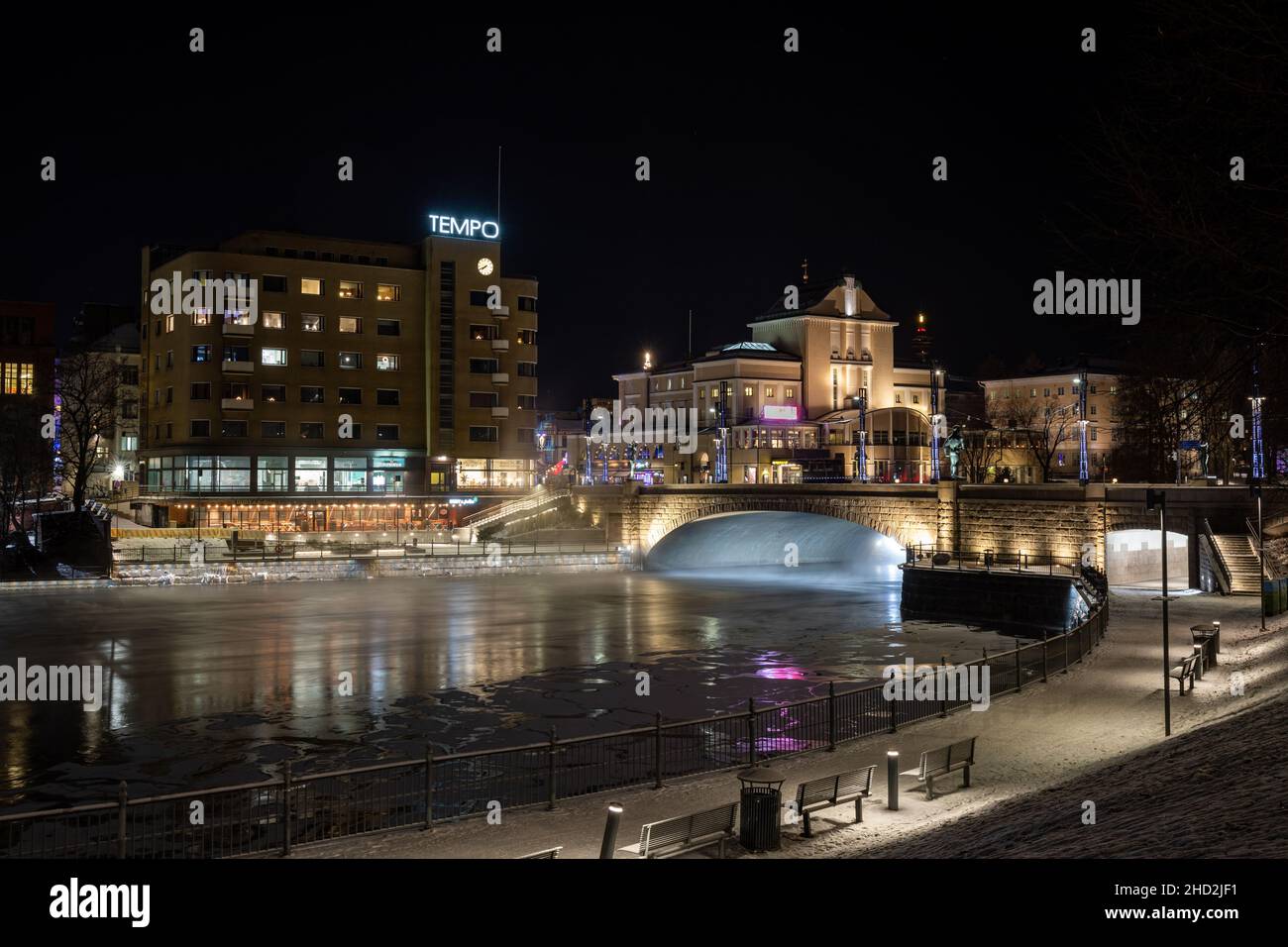 Beleuchtete Hämeensilta und die umliegenden Gebäude nach Einbruch der Dunkelheit in einer kalten Winternacht mit etwas Eis auf den Stromschnellen von Tammerkoski in Tampere, Finnland Stockfoto