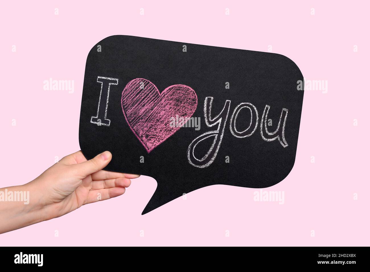 Weibliche Hand hält ein Schild mit der Kreideaufschrift „I love you“ und einem roten Herzen. Weihnachtsschriftzug zum Valentinstag. Stockfoto