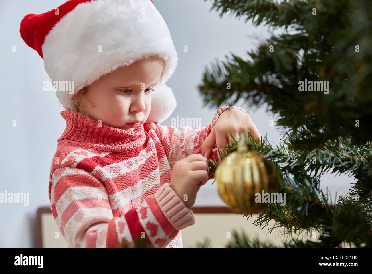 Mädchen in einem Weihnachtsmann Hut und einem Pullover mit einem Ornament sorgfältig verkleidet den Weihnachtsbaum. Das Konzept eines glücklichen neuen Jahres und Weihnachten. Lifestyle, Stockfoto