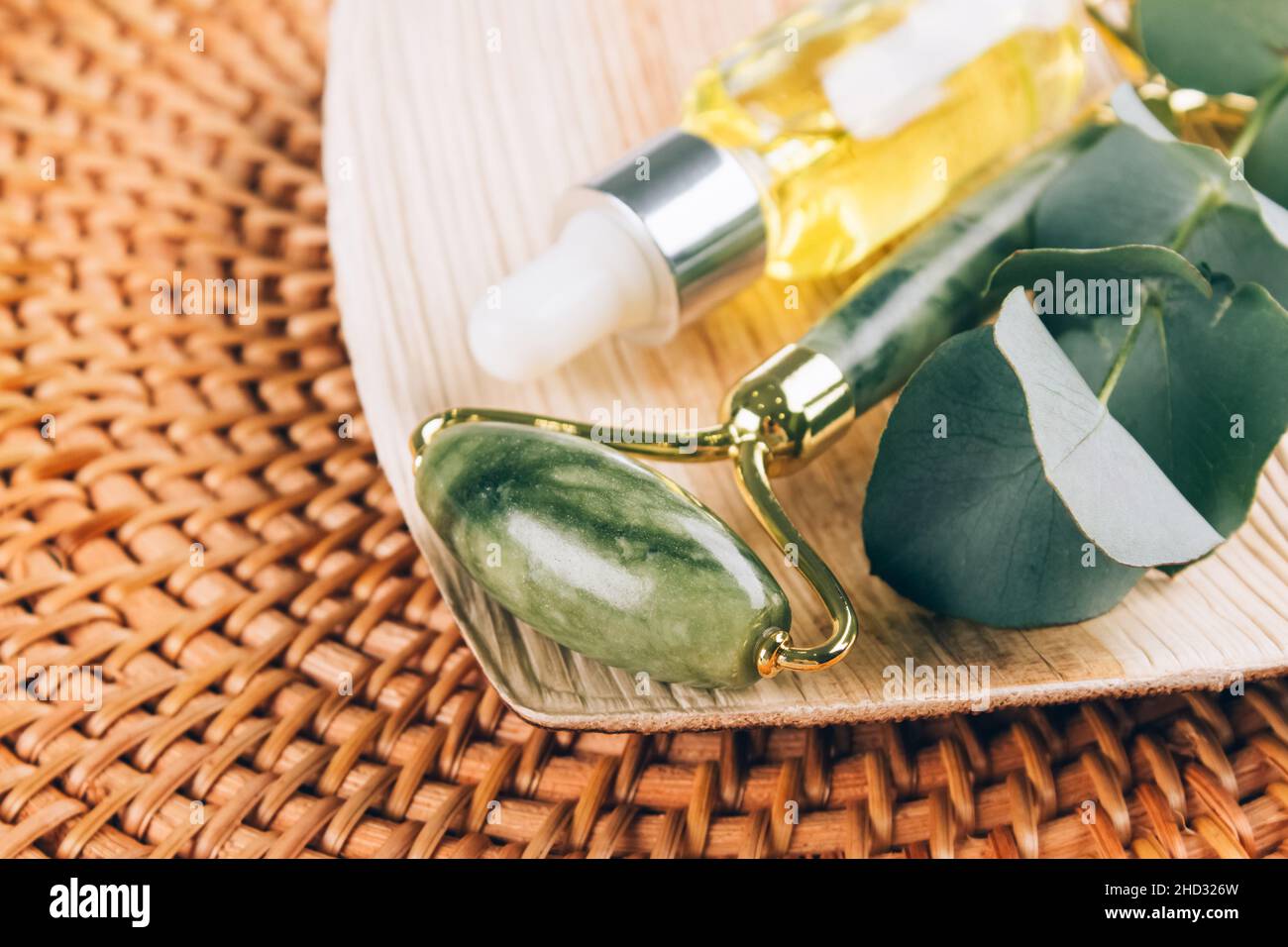 Nahaufnahme der Jade-Gesichtswalze mit Beauty-Serumöl auf natürlichem Strohgrund. Gesichtsmassage-Set für die Lifting-Massage-Therapie aus natura Stockfoto