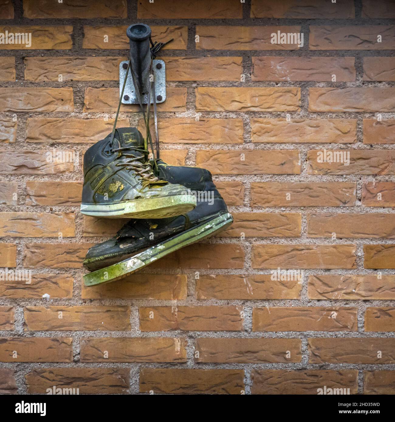 Schmutzige Schuhe, die auf einem Ziegelstein hängen Stockfoto