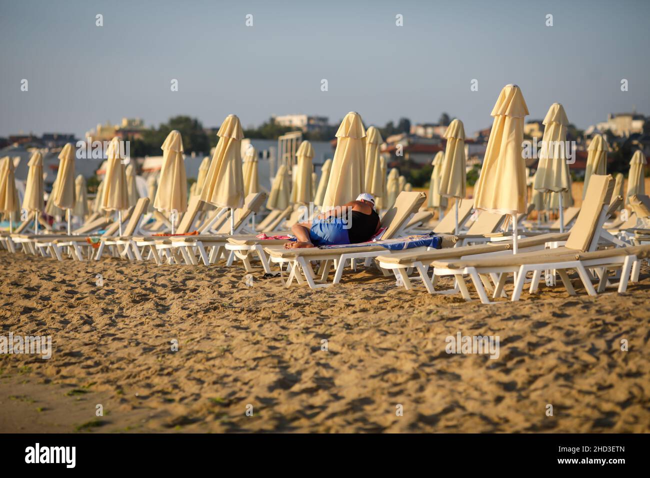 Mann sitzt auf einem Liegestuhl am Strand an einem ruhigen und warmen Sommermorgen am Schwarzen Meer im Obzor Resort in Bulgarien. Stockfoto