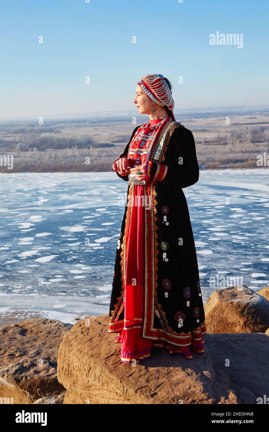 Im Winter steht eine junge Frau am Rand einer Klippe, gekleidet in ein nationales Baschkir-Kostüm. Stockfoto