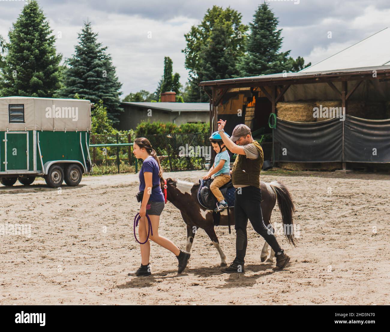 Kleiner Junge, der auf einem Pony reitet, während der Lehrer den Fußweg auf einer Pferdefarm führt Stockfoto