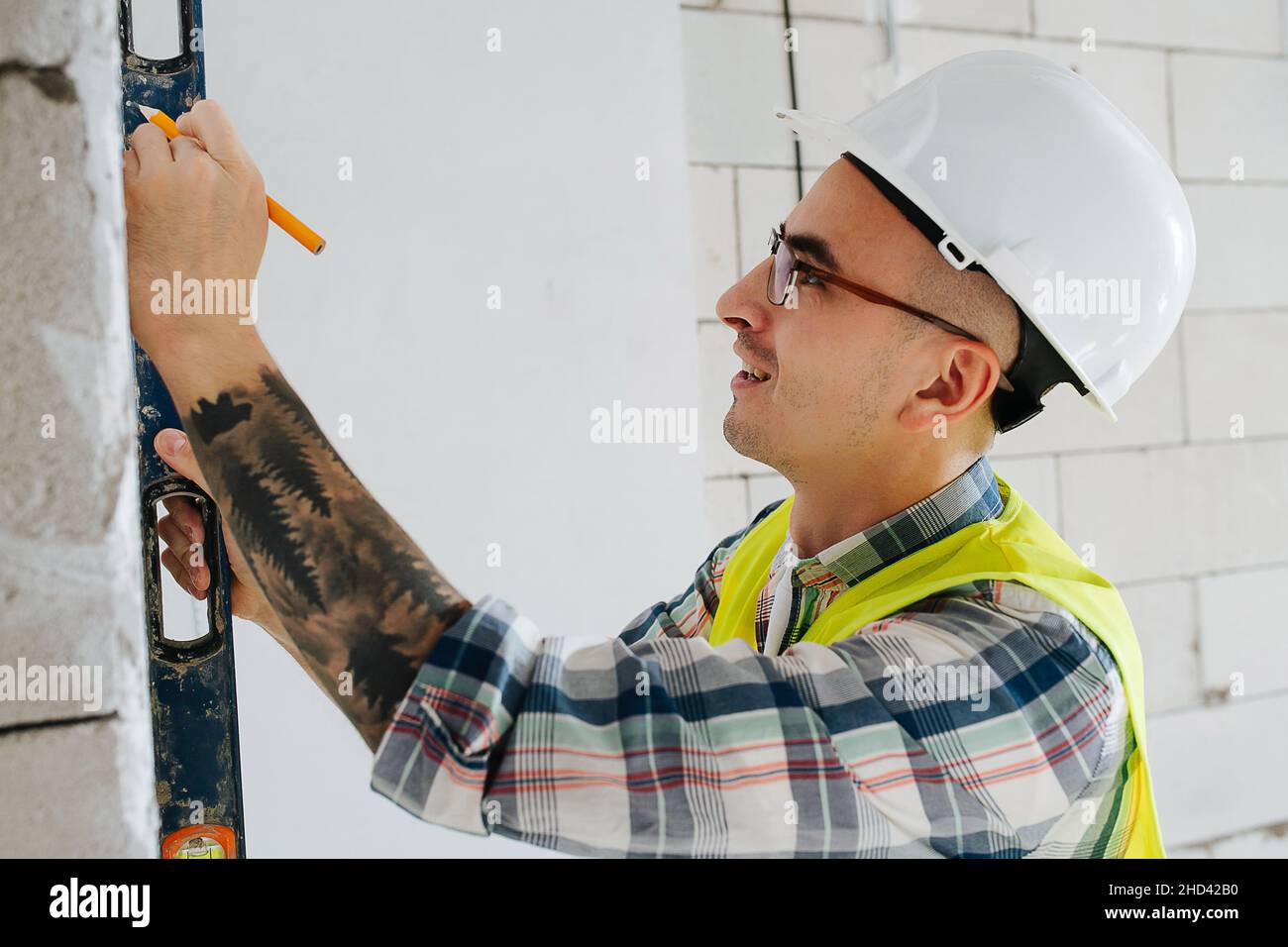 Skrupelloser Bauingenieur in einem weißen Helm, der in einem unfertigen Gebäude Markierungen an einer Ziegelmauer macht. Stockfoto