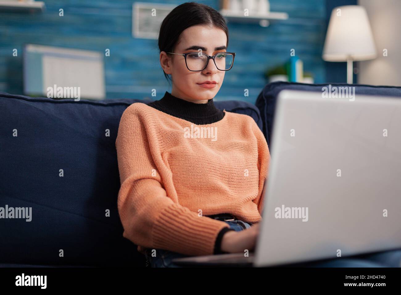 Programmierer mit Brille, die Laptop auf Sofa hält, um Code zu schreiben. Inhaltsersteller tippt im Büro zu Hause im Wohnzimmer. Student auf dem Sofa, der sich die Bildschirmanzeige in den sozialen Medien ansieht. Stockfoto