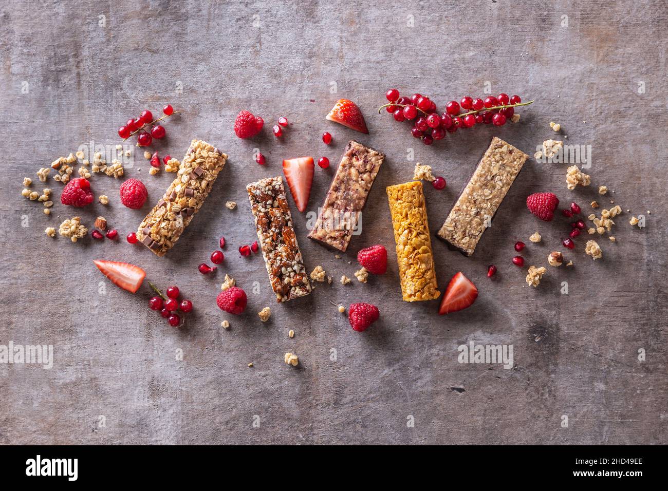 Verschiedene Müsliriegel mit Johannisbeeren, Himbeeren und Erdbeeren sowie Getreide um sie herum, von oben betrachtet. Stockfoto