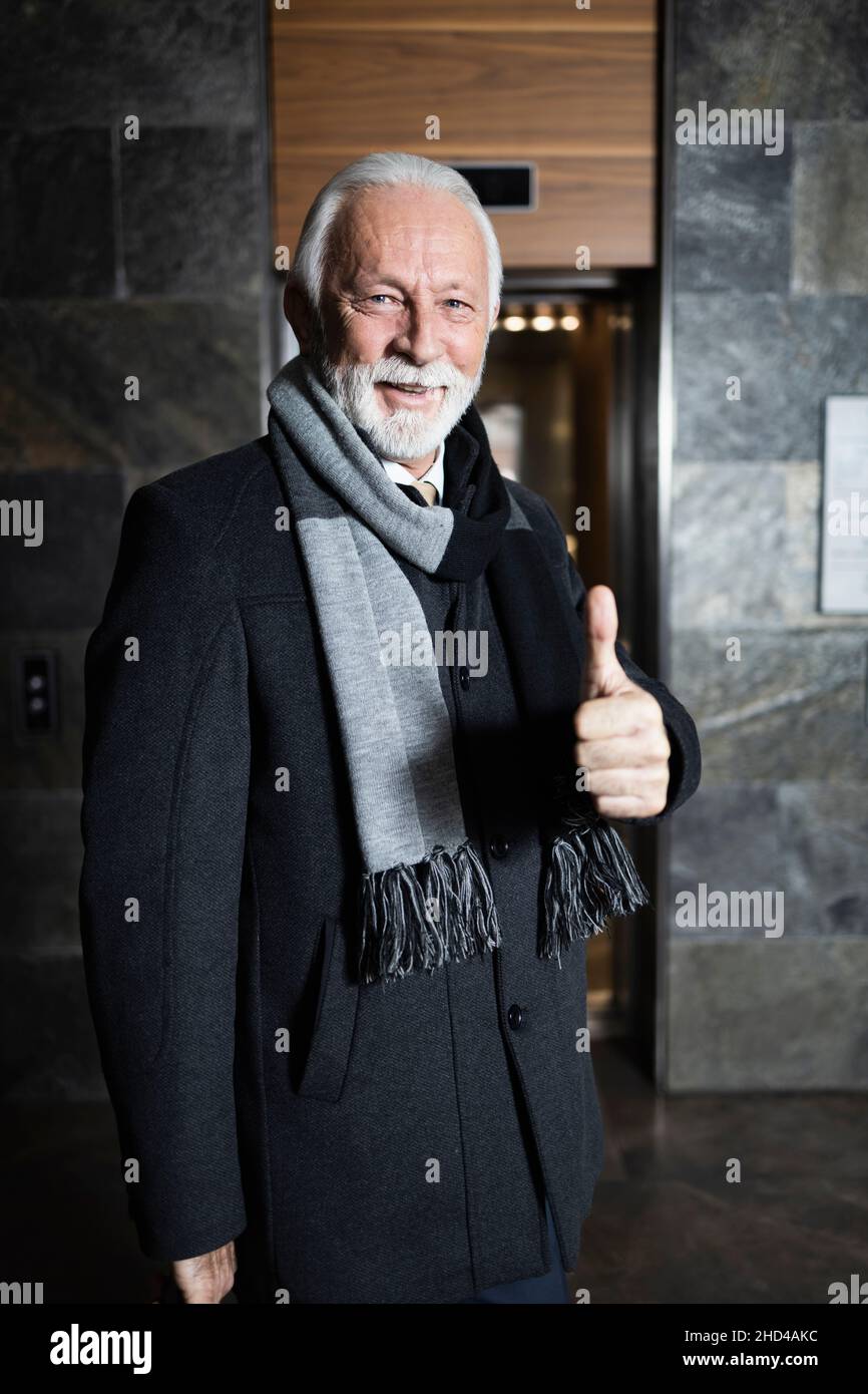 Ein älterer, eleganter Mann zeigt den Daumen nach oben in der Hotellobby Stockfoto