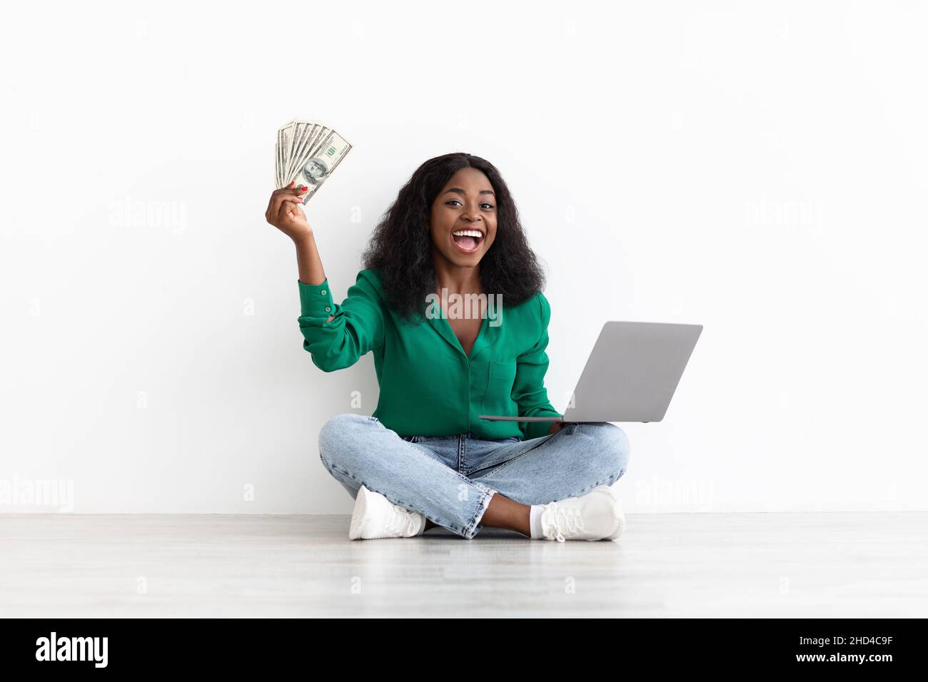 Reiche afroamerikanische Dame spielt online, hält Laptop und Geld Stockfoto