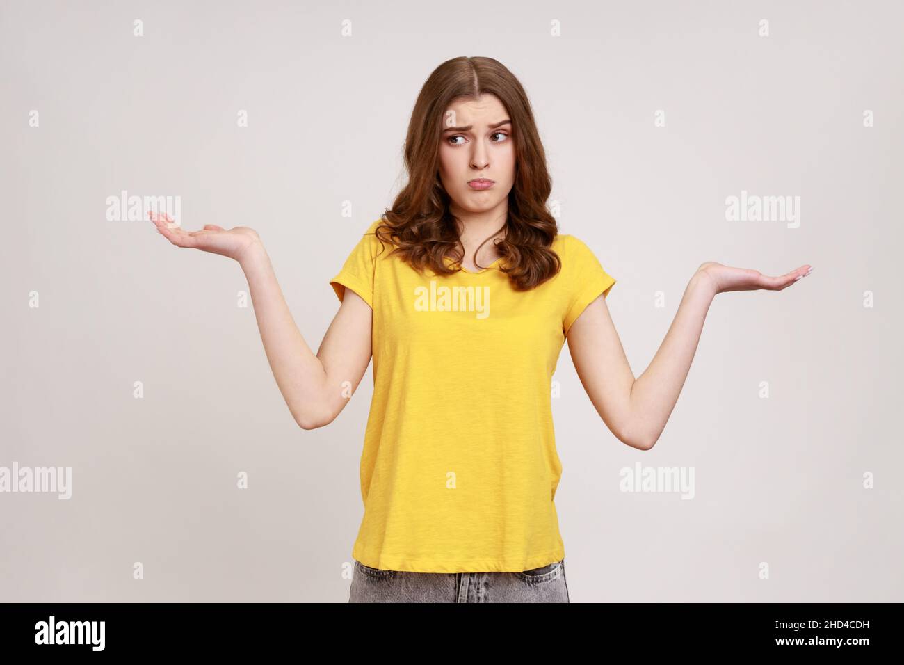 Ich weiß nicht, wen kümmert das schon. Porträt von verwirrt ahnungslos attraktive Teenager-Mädchen in gelben T-Shirt zuckende Schultern, so dass keine Idee Geste, was auch immer. Innenaufnahme des Studios isoliert auf grauem Hintergrund. Stockfoto