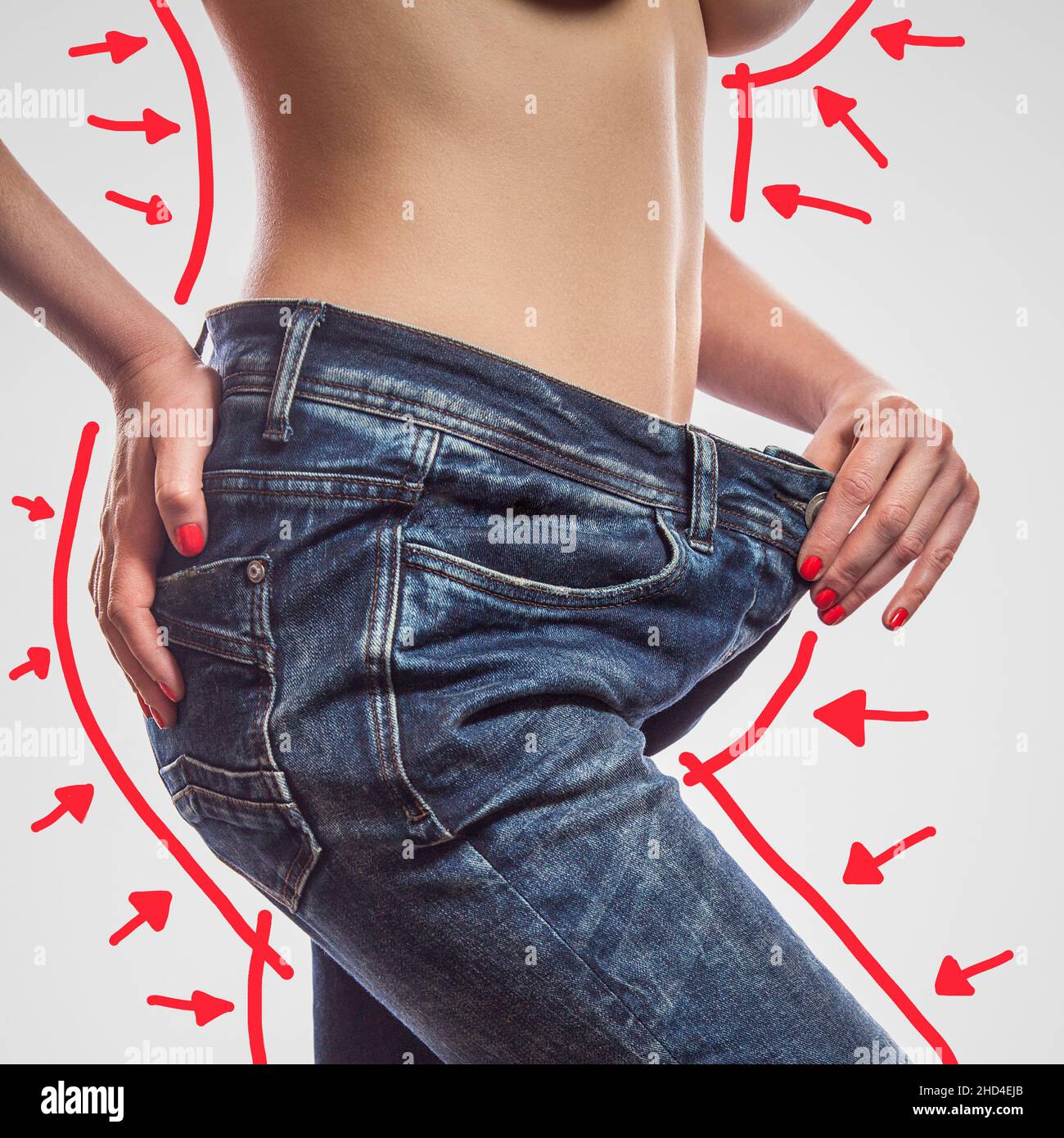 Nahaufnahme einer schlanken Taille einer jungen Frau, die in einer großen Jeans steht und eine erfolgreiche Gewichtsabnahme zeigt, Aufnahme in einem Studio, isoliert auf hellgrauem Hintergrund, Diätkonzept. Stockfoto