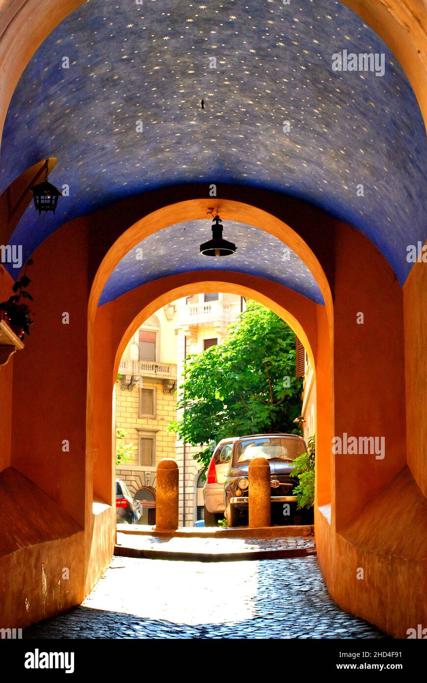 Blick auf eine malerische Straße mit einem Bogen in Rom-Stadt, Italien mit orangefarbenen Wänden und einer blauen Decke Stockfoto