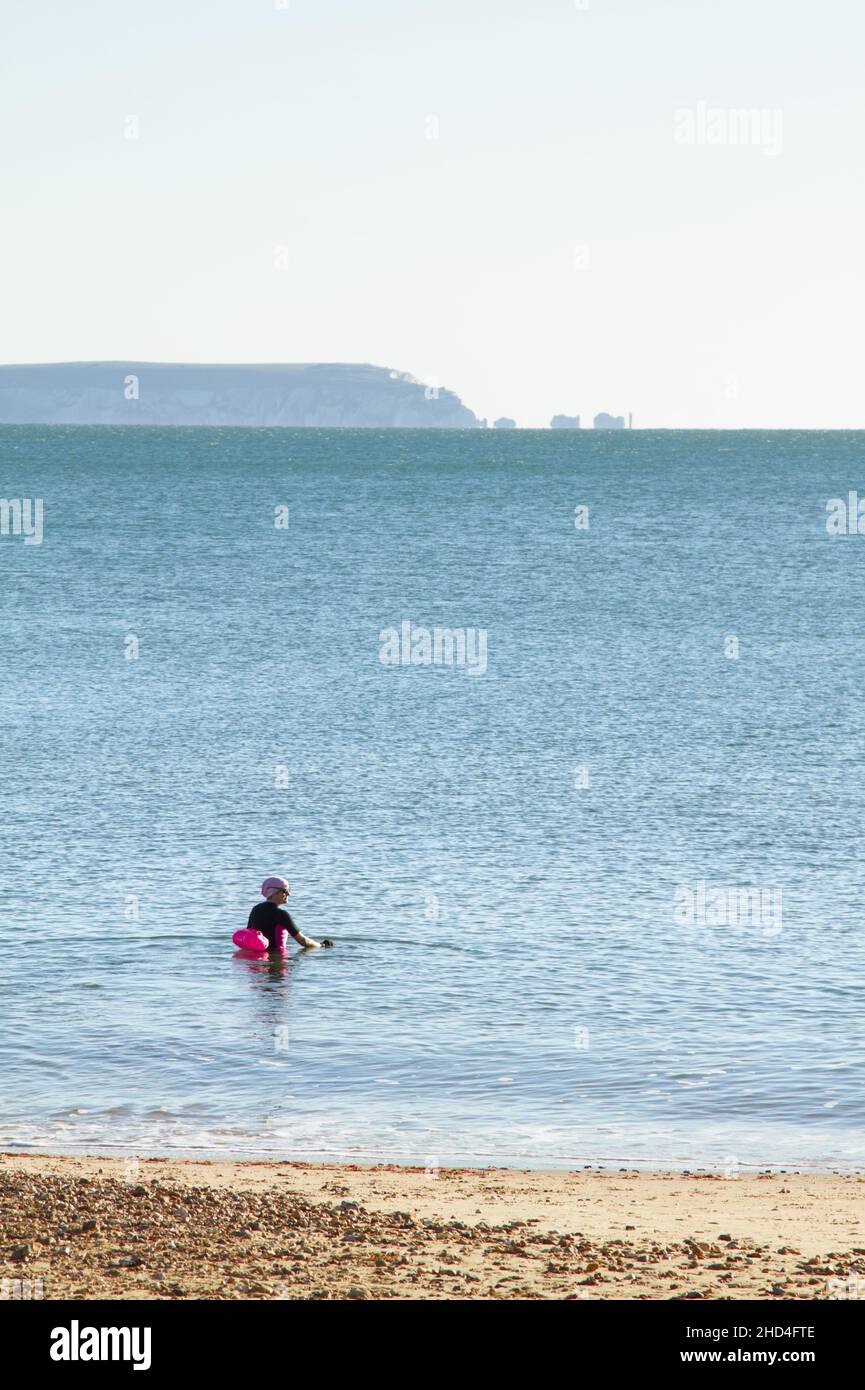 Weibliche Wildschwimmerin Schwimmen im Meer im Winter vor Avon Beach mit Blick über den Solent in Richtung Isle of Wight und die Needles UK Stockfoto