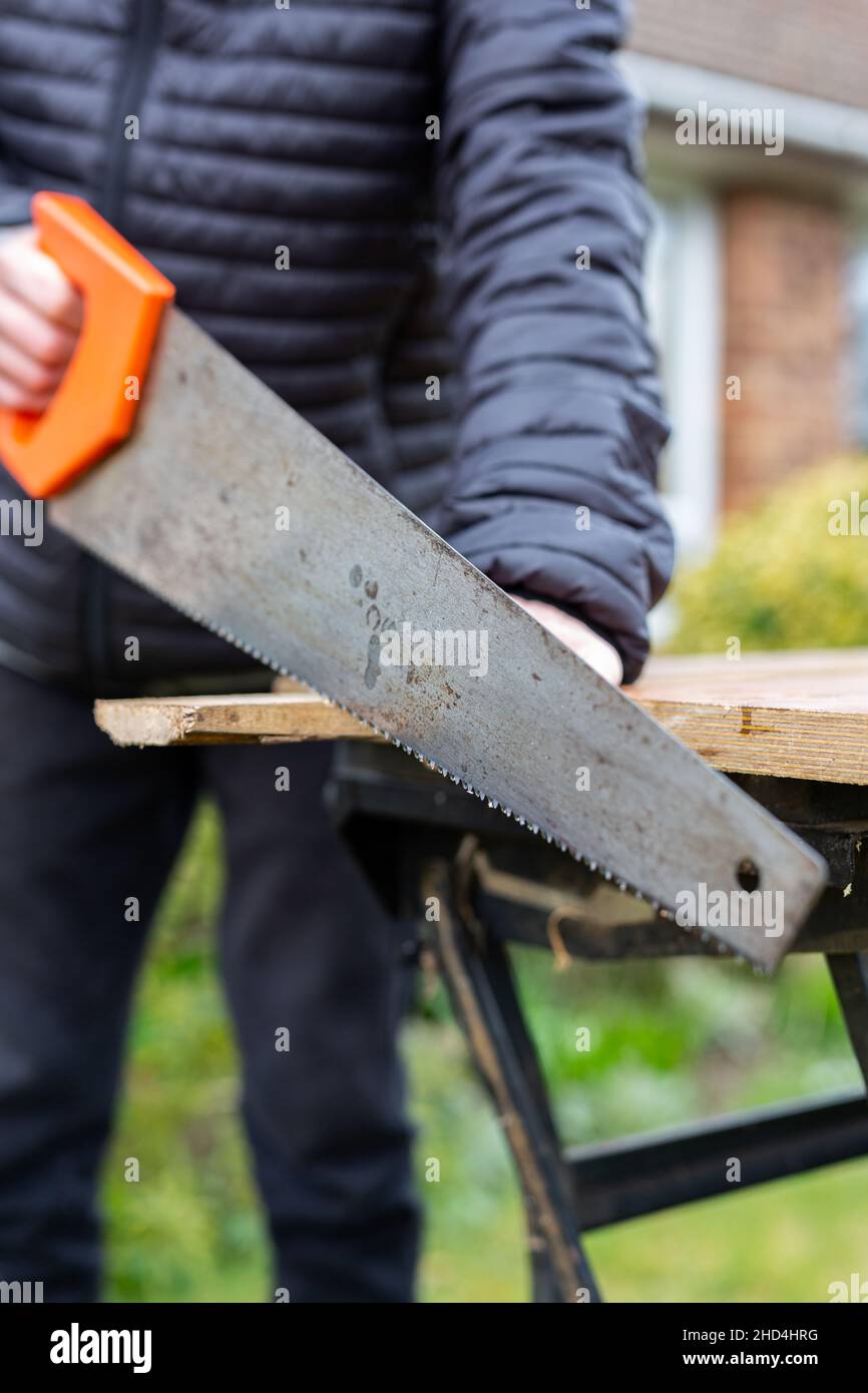 Nahaufnahme einer unbekannten Person mit einer Handsäge, um ein Holzbrett zu schneiden. DIY, Bau, Heimwerkerkonzept Stockfoto