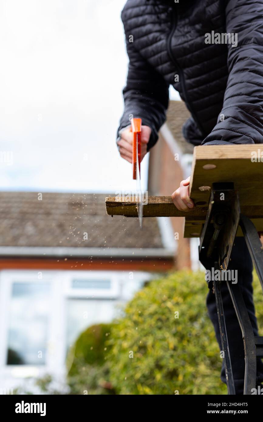 Nahaufnahme einer unbekannten Person mit einer Handsäge, um ein Holzbrett zu schneiden. DIY, Bau, Heimwerkerkonzept Stockfoto
