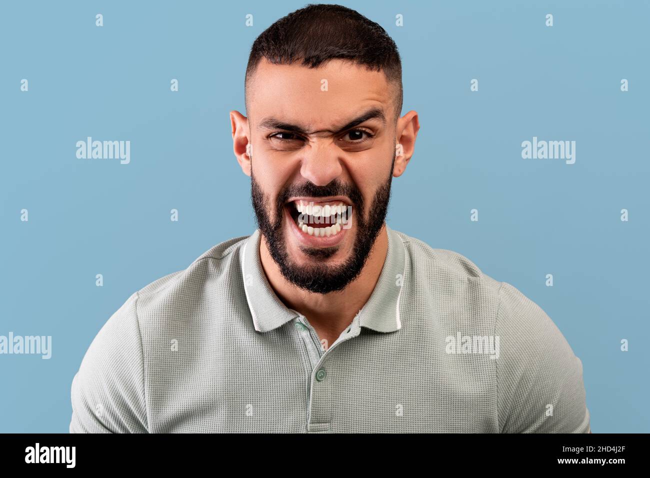 Porträt eines wütenden arabischen Mannes, der vor Wut auf die Kamera schreit, vor Wut schreit und auf blauem Hintergrund steht Stockfoto