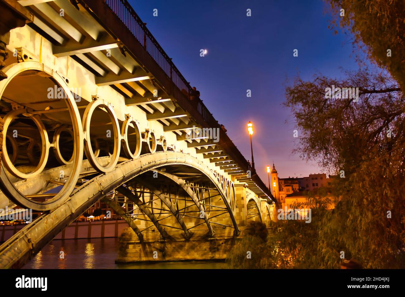 Nachtfoto der Triana Brücke mit Straßenlaternen und Reflexionen im Wasser, Sevilla,Andalusien, Spanien. Stockfoto