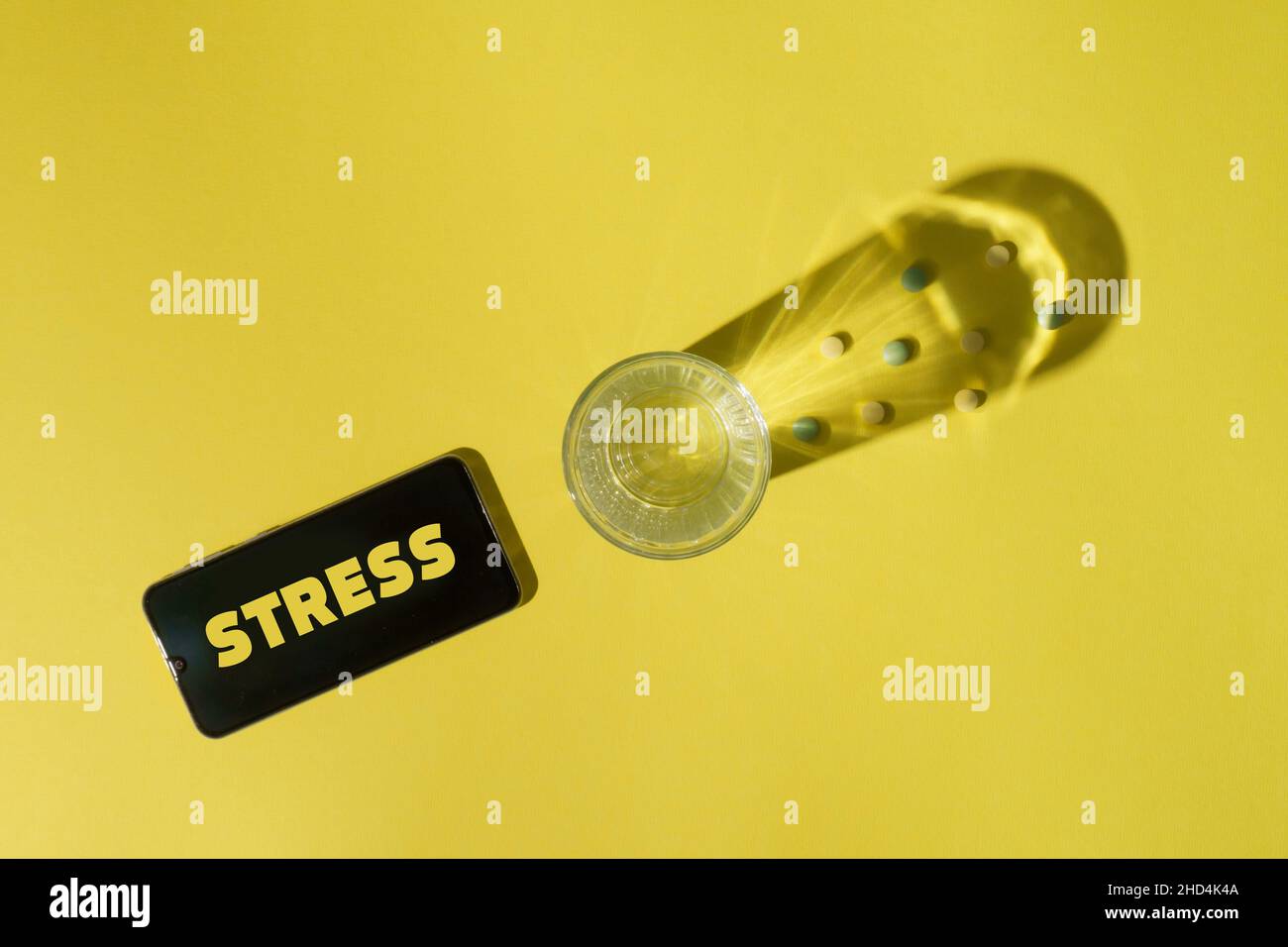 Pillen, Glas Wasser und Smartphone auf gelbem Hintergrund. Stress und Depression Konzept Stockfoto