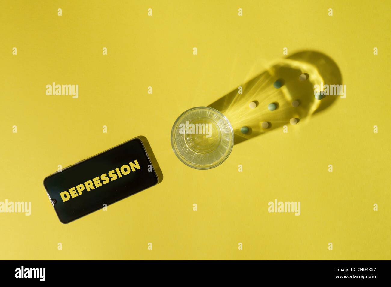 Pillen, Glas Wasser und Smartphone auf gelbem Hintergrund. Stress und Depression Konzept Stockfoto