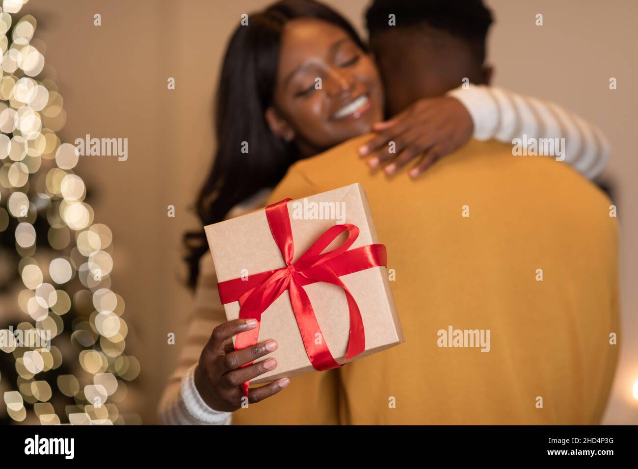 Schwarzes Paar Umarmt Holding Geschenk In Der Nähe Von Weihnachtsbaum Indoor Stehen Stockfoto