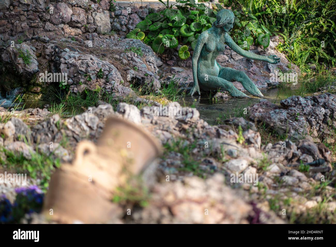 Bronzestatue einer Frau, die in einem griechischen Garten auf einem Felsen sitzt Stockfoto