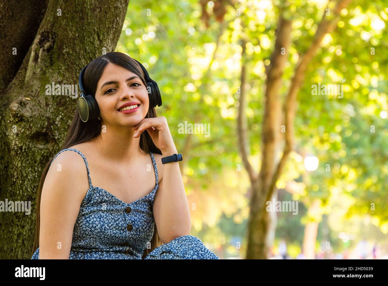 Junge Frau im Park, die während der Sommerfrühlingszeit Kopfhörer verwendet, um an sonnigen Tagen Musik zu hören Stockfoto