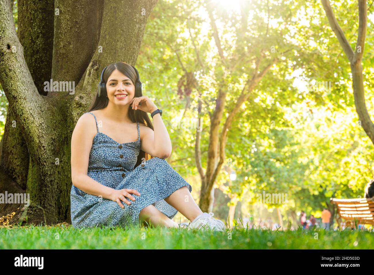 Junge Frau im Park, die während der Sommerfrühlingszeit Kopfhörer verwendet, um an sonnigen Tagen Musik zu hören Stockfoto