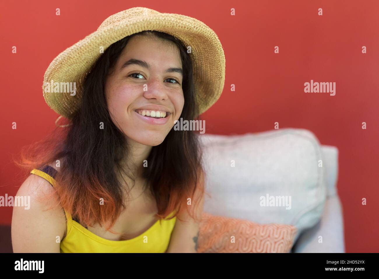 Junge lächelnde Frau im Strohhut posiert für ein Foto mit rotem Hintergrund Stockfoto