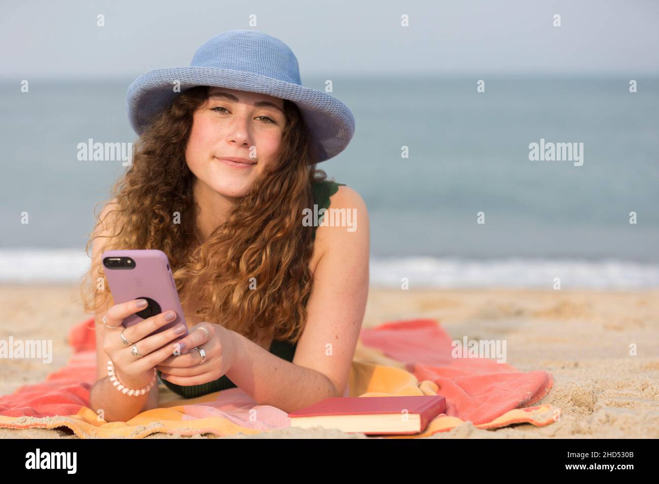 Junge Frau am Strand auf einem Handtuch mit dem Handy. Stockfoto