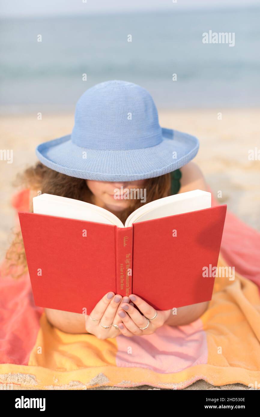 Junge Frau am Strand auf einem Handtuch beim Lesen eines Buches Stockfoto