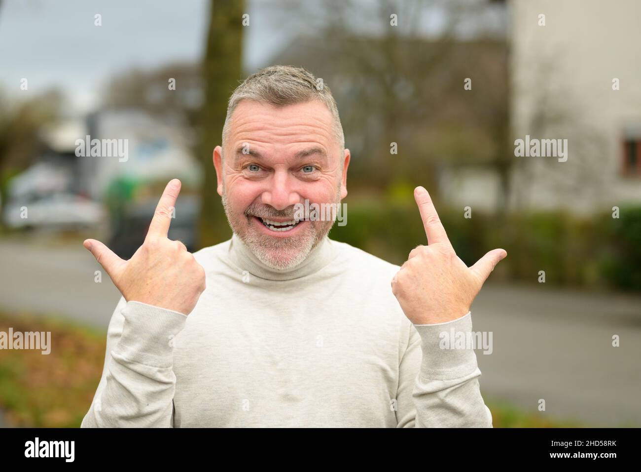 Ein fröhlich-beschwingter Mann grinst die Kamera an, während er mit beiden Händen gestikulierte, um seinen Erfolg auf einer ruhigen Straße in der Stadt im Freien zu zeigen Stockfoto