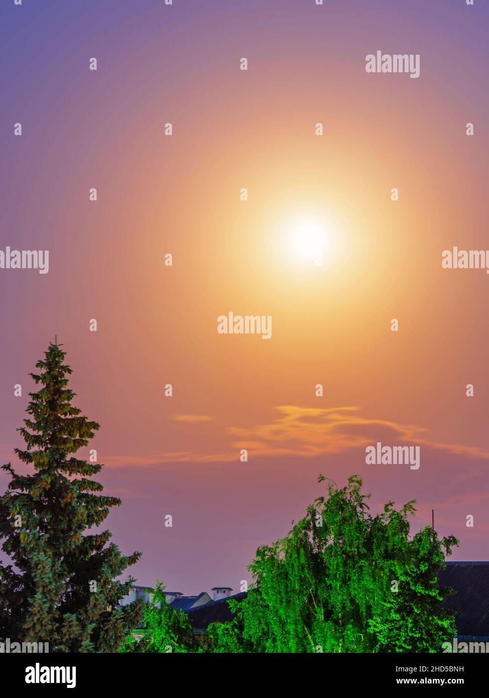 Mond und diffuses Mondlicht in einem violetten Himmel unter den Dächern von Häusern und Bäumen Stockfoto